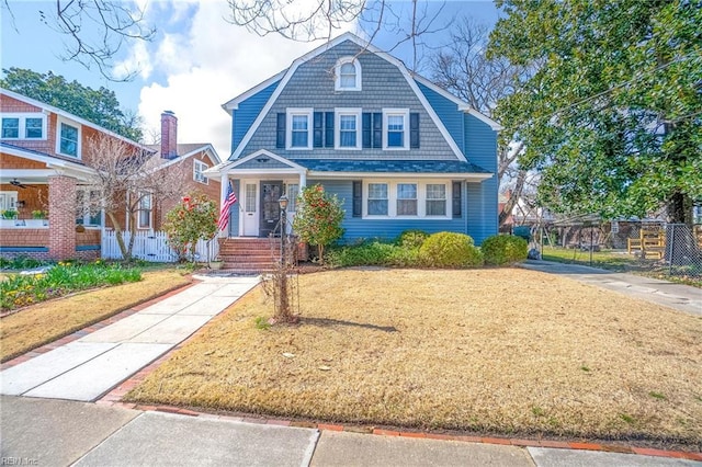 shingle-style home featuring a gambrel roof, concrete driveway, a front yard, and fence