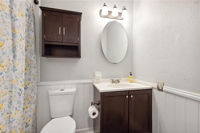 bathroom with vanity, curtained shower, toilet, and wainscoting