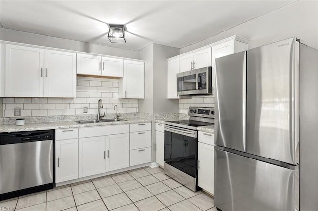 kitchen with a sink, tasteful backsplash, appliances with stainless steel finishes, white cabinets, and light stone countertops