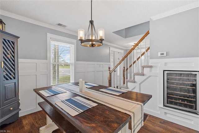 dining area featuring visible vents, dark wood-type flooring, wine cooler, an inviting chandelier, and crown molding