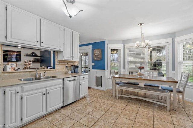 kitchen with a sink, light countertops, white cabinets, stainless steel dishwasher, and a notable chandelier