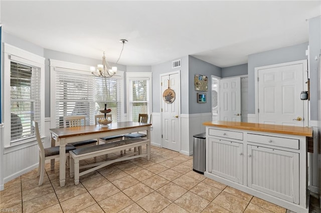 dining space featuring a wainscoted wall, a notable chandelier, light tile patterned flooring, and visible vents