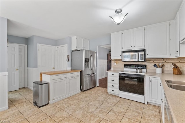 kitchen with white cabinetry, light tile patterned floors, wainscoting, and stainless steel appliances