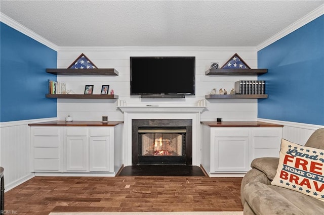 living room with dark wood-type flooring, ornamental molding, wainscoting, a fireplace, and a textured ceiling