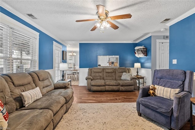 living area featuring visible vents, ceiling fan with notable chandelier, a textured ceiling, wood finished floors, and crown molding