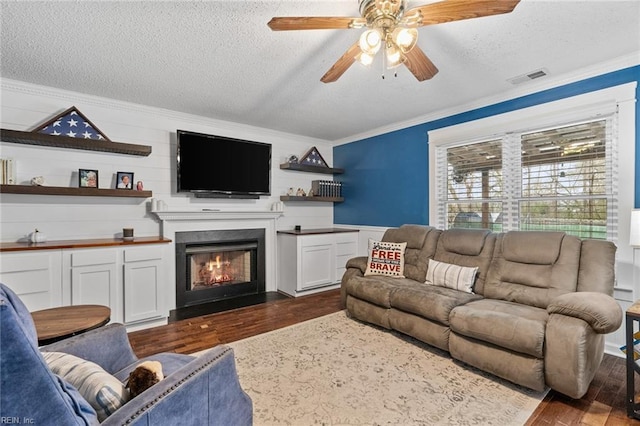 living room featuring visible vents, ceiling fan, ornamental molding, a textured ceiling, and dark wood-style flooring