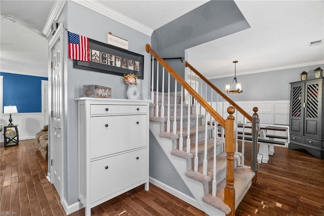 staircase with visible vents, a notable chandelier, ornamental molding, wood finished floors, and wainscoting