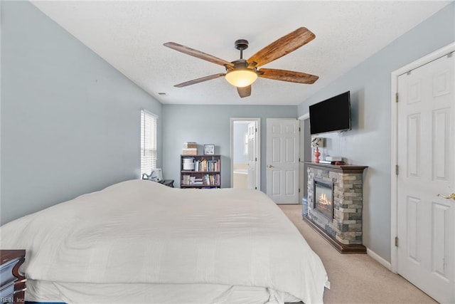 bedroom with a ceiling fan, a textured ceiling, ensuite bath, a fireplace, and light colored carpet