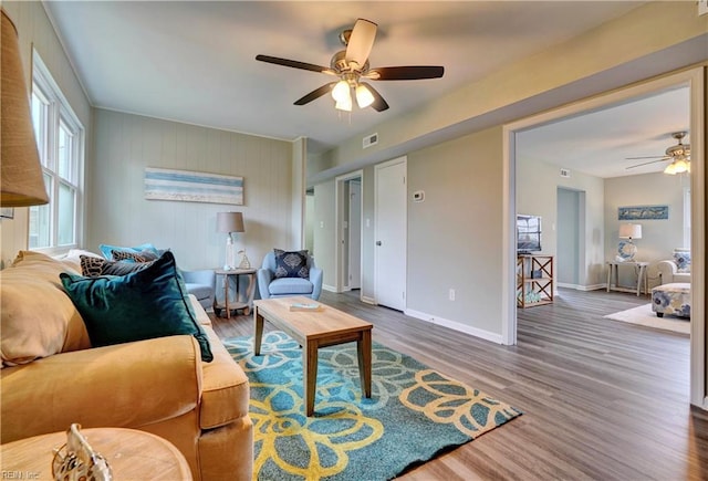 living area featuring baseboards, wood finished floors, visible vents, and ceiling fan