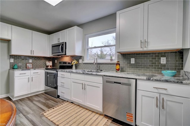 kitchen with light wood-type flooring, a sink, light stone counters, stainless steel appliances, and white cabinets