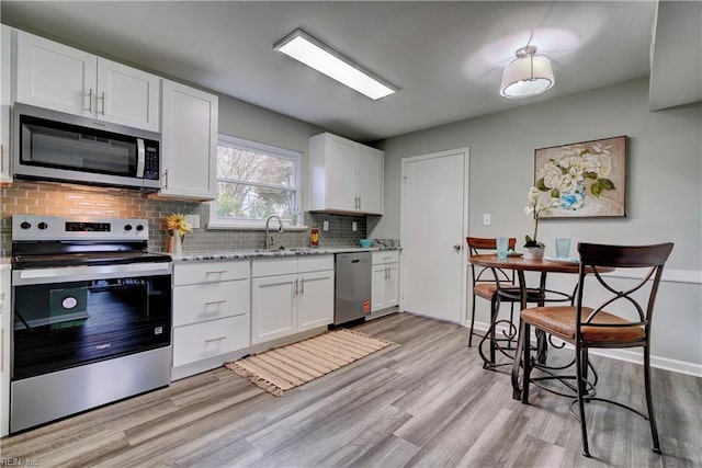 kitchen with decorative backsplash, appliances with stainless steel finishes, light wood-style floors, white cabinets, and a sink