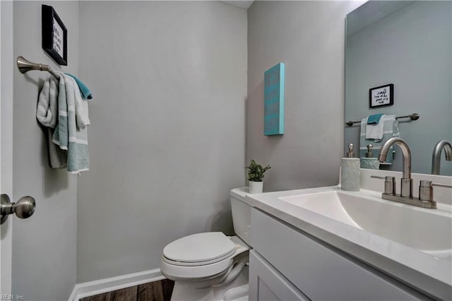 half bathroom featuring vanity, toilet, wood finished floors, and baseboards