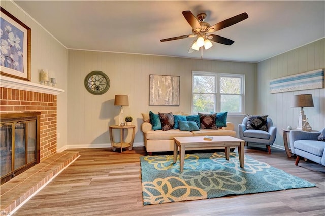 living area featuring ceiling fan, baseboards, wood finished floors, and a fireplace