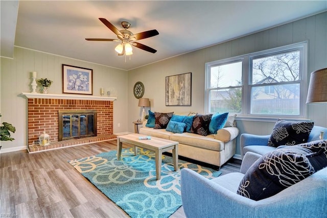 living room with ceiling fan, baseboards, a brick fireplace, and wood finished floors