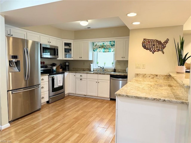 kitchen featuring light wood finished floors, recessed lighting, a sink, stainless steel appliances, and white cabinetry