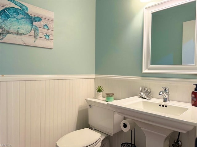 half bathroom featuring toilet, a wainscoted wall, and a sink