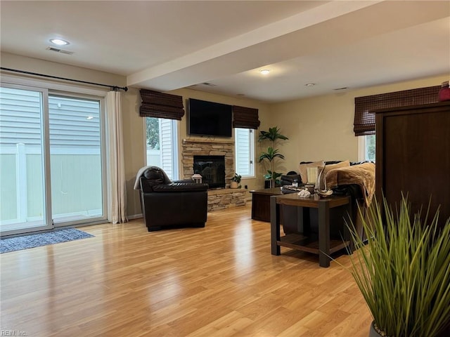 living room with light wood finished floors, visible vents, a healthy amount of sunlight, and a stone fireplace