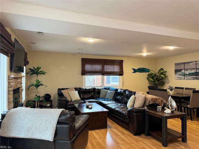 living area featuring a stone fireplace, light wood-style floors, and visible vents