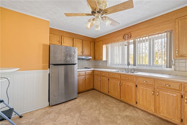 kitchen featuring a wainscoted wall, a sink, under cabinet range hood, freestanding refrigerator, and light countertops