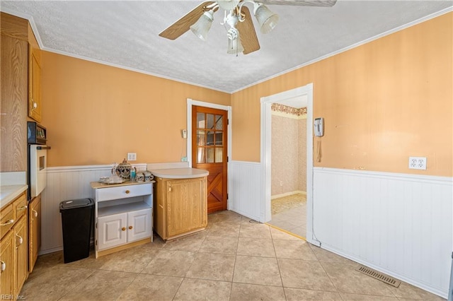 kitchen with visible vents, a wainscoted wall, light tile patterned flooring, oven, and light countertops