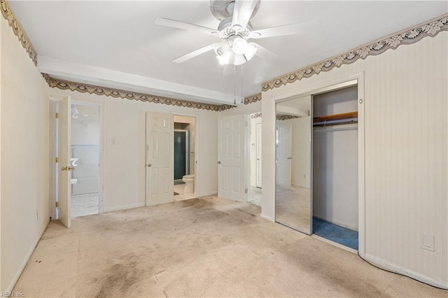 unfurnished bedroom featuring a closet, carpet flooring, connected bathroom, and ceiling fan