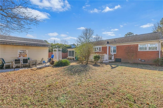 back of house with crawl space, a yard, brick siding, and a patio area