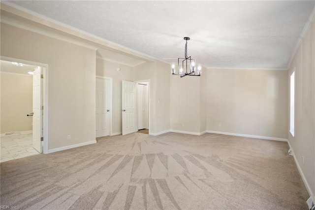 carpeted spare room featuring a chandelier, a textured ceiling, baseboards, and ornamental molding