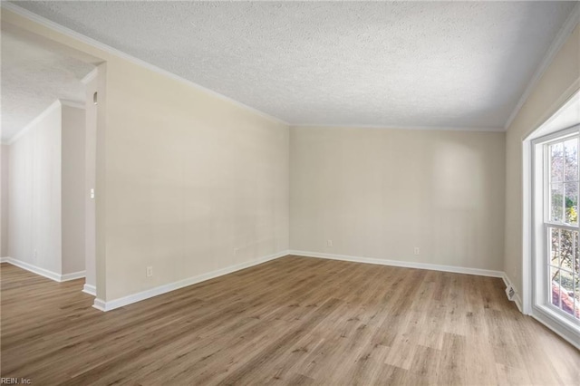 empty room featuring light wood finished floors, a textured ceiling, crown molding, and baseboards