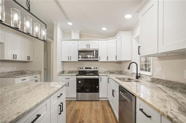 kitchen with a sink, white cabinetry, stainless steel appliances, light wood finished floors, and hanging light fixtures