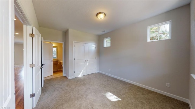 unfurnished bedroom with light carpet, a closet, ensuite bath, and baseboards