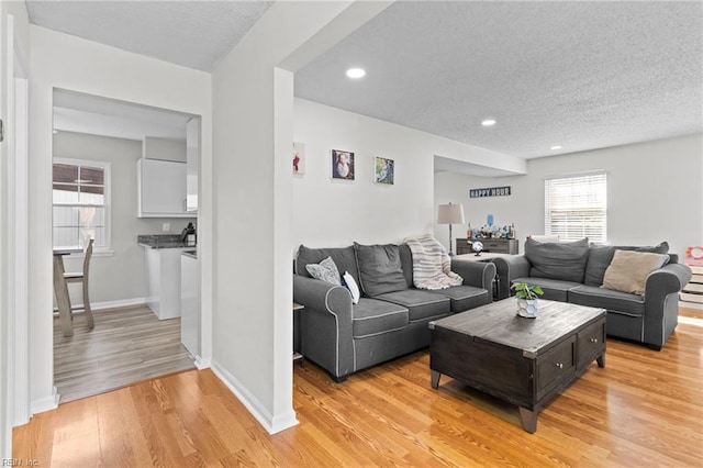 living room with recessed lighting, baseboards, a textured ceiling, and light wood-style flooring