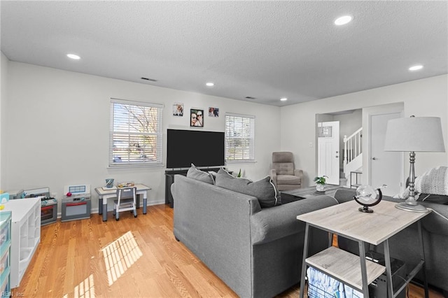 living area with recessed lighting, light wood-type flooring, a textured ceiling, and stairway