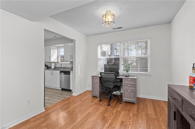 home office with visible vents, light wood-style flooring, baseboards, and a healthy amount of sunlight