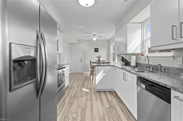 kitchen with light wood-style flooring, a ceiling fan, a sink, dark stone counters, and appliances with stainless steel finishes