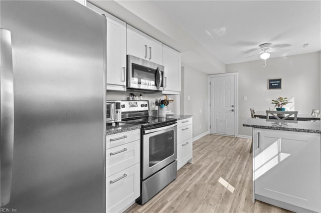 kitchen with dark stone countertops, ceiling fan, white cabinets, light wood-style floors, and appliances with stainless steel finishes