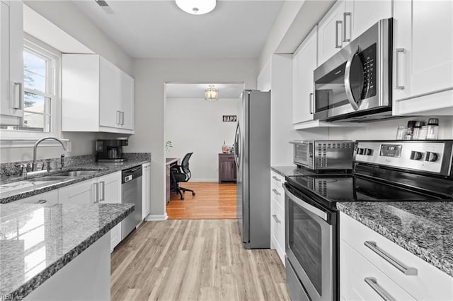 kitchen with white cabinets, appliances with stainless steel finishes, light wood-style floors, and a sink