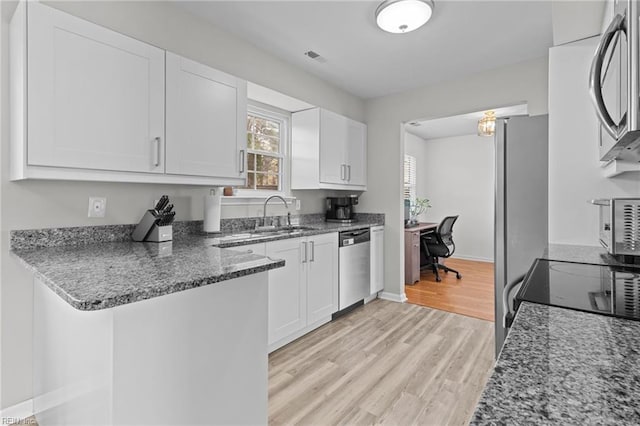 kitchen with light wood finished floors, dark stone countertops, stainless steel appliances, white cabinetry, and a sink