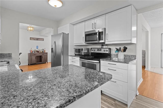 kitchen with light wood-style flooring, appliances with stainless steel finishes, a peninsula, dark stone countertops, and white cabinets