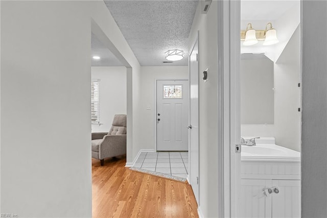 foyer featuring light wood-type flooring, baseboards, and a textured ceiling