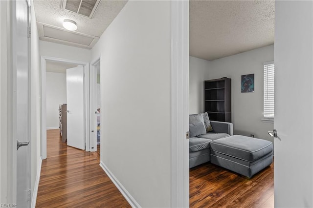 hallway featuring attic access, visible vents, dark wood-style flooring, and a textured ceiling