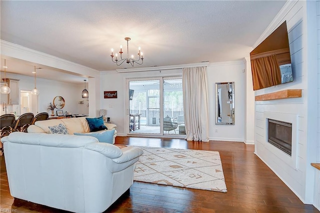 living area featuring dark wood-style floors, a fireplace, ornamental molding, a textured ceiling, and a notable chandelier