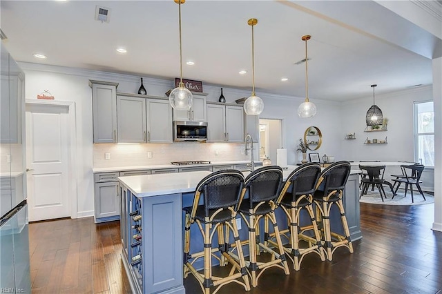 kitchen with dark wood-type flooring, crown molding, a breakfast bar, light countertops, and appliances with stainless steel finishes