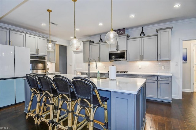 kitchen featuring a center island with sink, dark wood finished floors, gray cabinets, appliances with stainless steel finishes, and backsplash