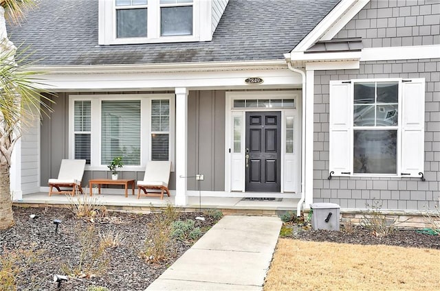 doorway to property with a porch, board and batten siding, and roof with shingles