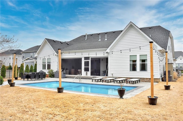 rear view of property featuring a lawn, an outdoor pool, a shingled roof, and a patio