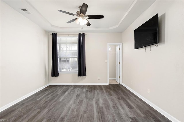 empty room featuring visible vents, a ceiling fan, a tray ceiling, wood finished floors, and baseboards