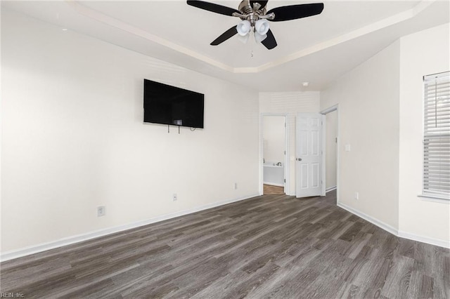 interior space featuring a raised ceiling, a ceiling fan, ensuite bath, wood finished floors, and baseboards