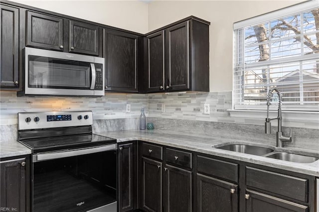 kitchen with backsplash, light stone countertops, appliances with stainless steel finishes, dark cabinetry, and a sink