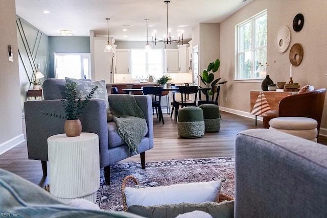 living area with a wealth of natural light, a notable chandelier, baseboards, and dark wood-type flooring