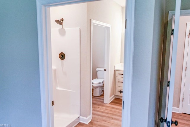 bathroom featuring wood finished floors, toilet, a stall shower, and vanity